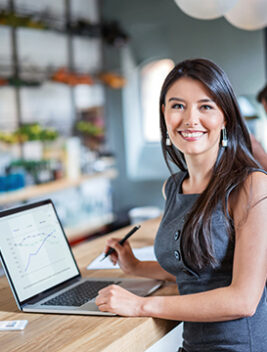Happy business woman working at a cafe on a laptop and looking at the camera smiling. Image on screen is own design.